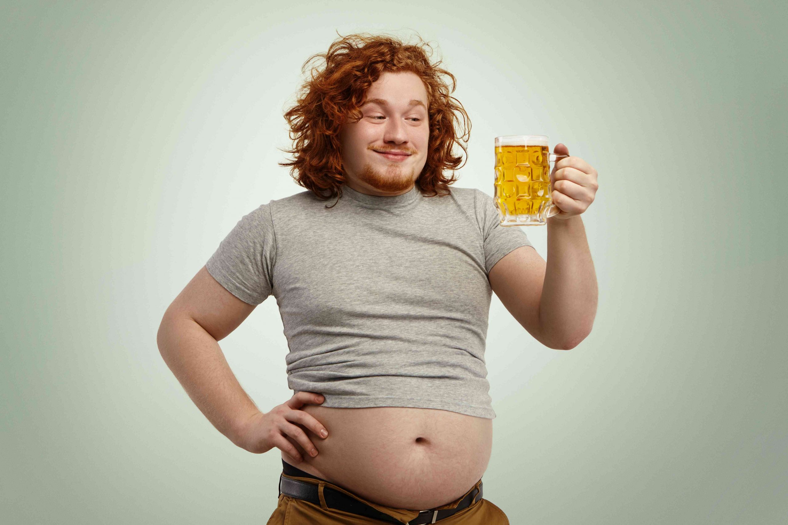 man holding beer in beer mug and showing off a huge beer belly