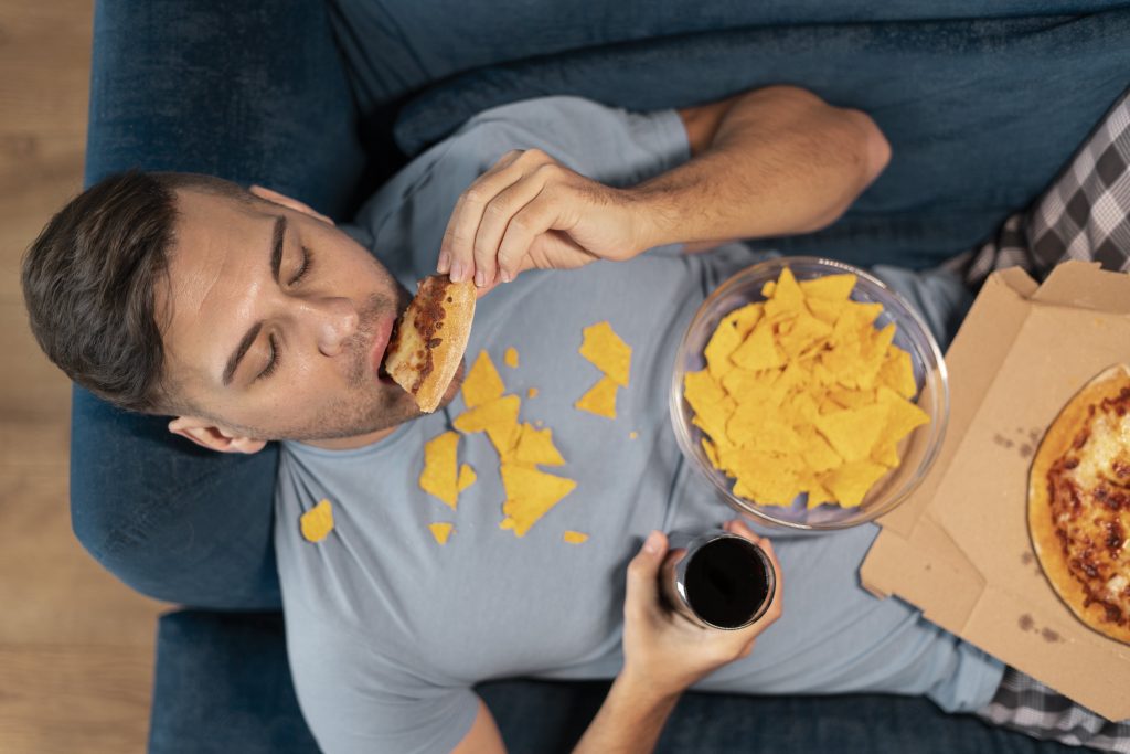 A man is binge eating while lying in a sofa.