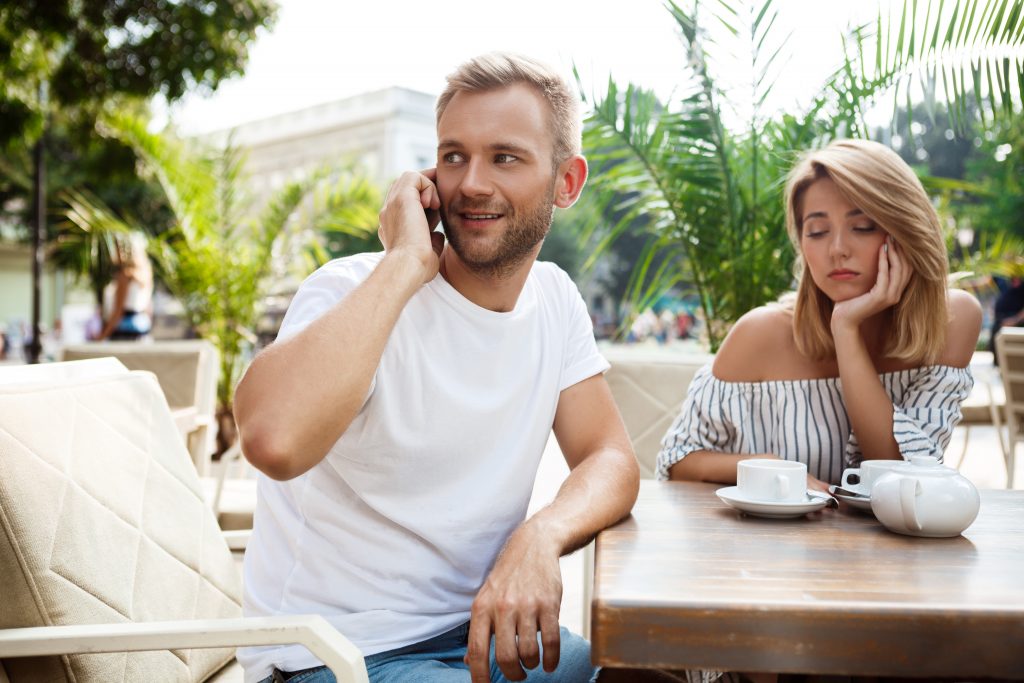 a person talking on a cell phone while sitting at a table with a person
