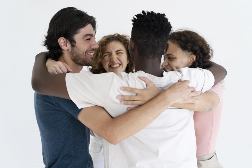 a group of friends from various ethnic background hug and laugh together