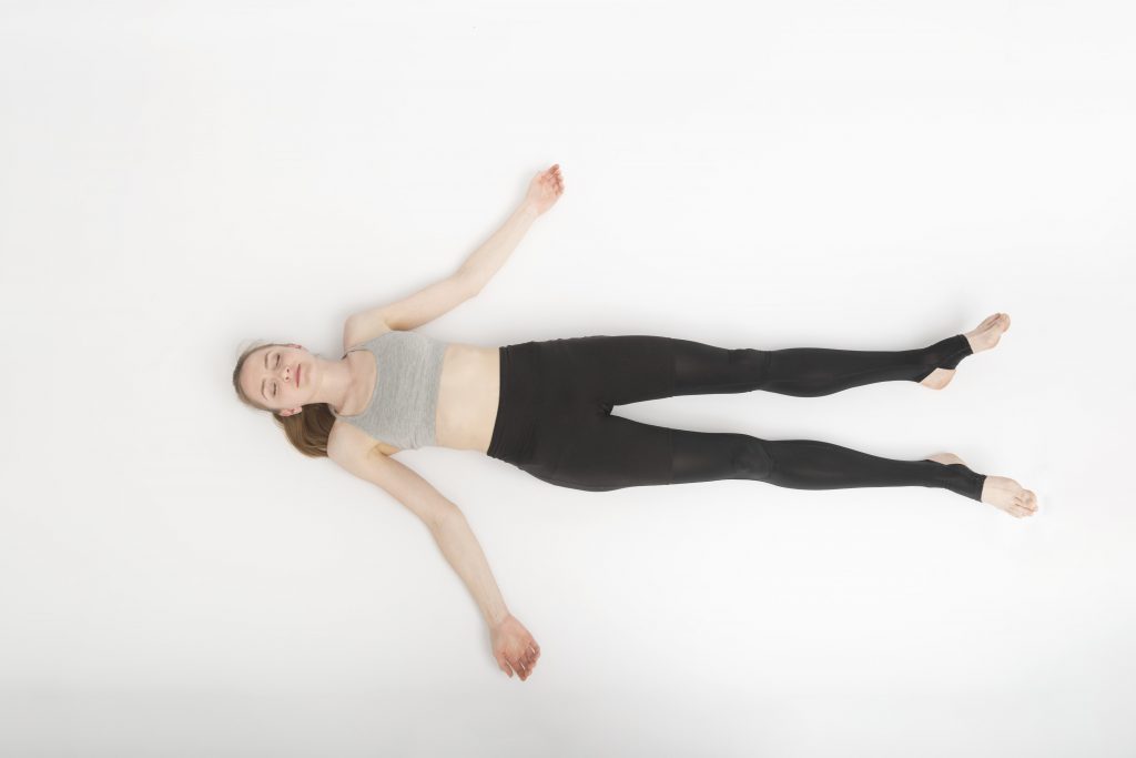 woman lying in shavasana, legs wider on the floor and arms relaxed, eyes closed