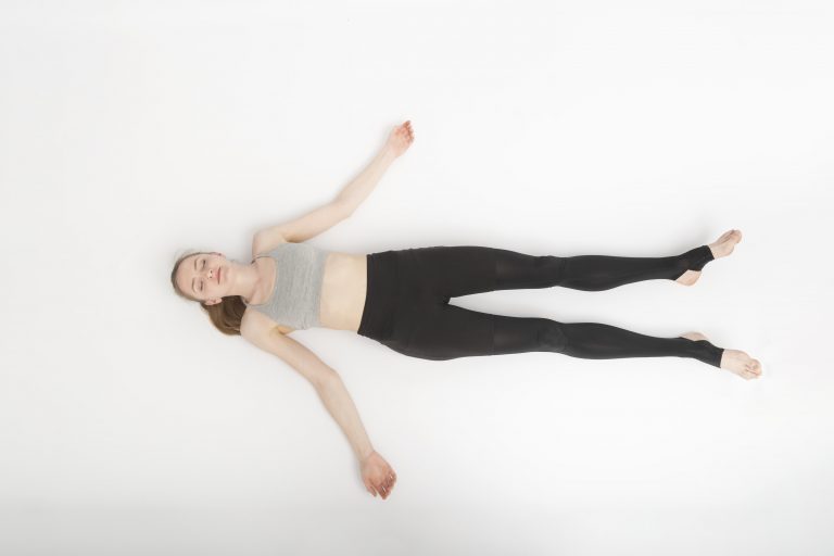 woman lying in shavasana, legs wider on the floor and arms relaxed, eyes closed