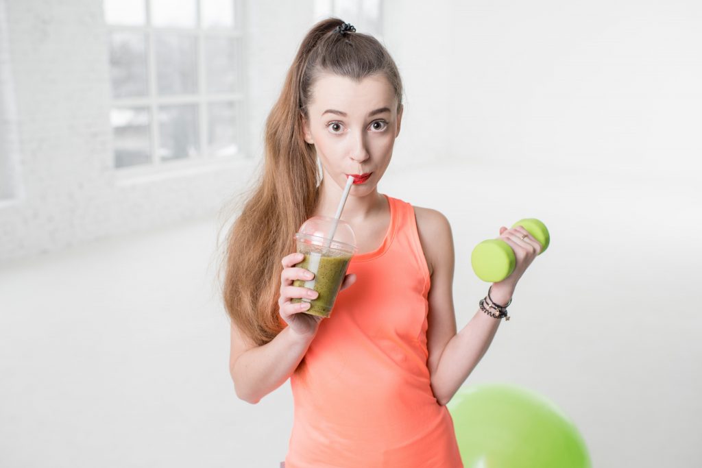 beautiful girl holding a dumbbell in one hand and drinking a healthy green juice with the other hand