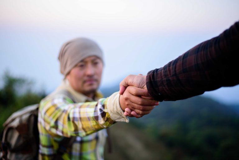 one man giving a helping hand to the other man while climbing up a hill