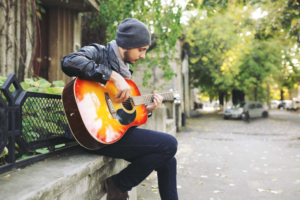 A man sitting on a sideway and playing his guitar.