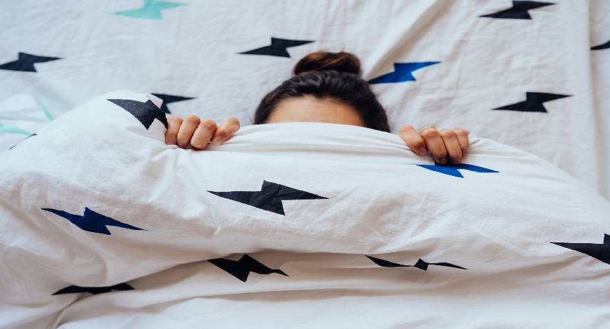 girl covering her face with blanket on bed