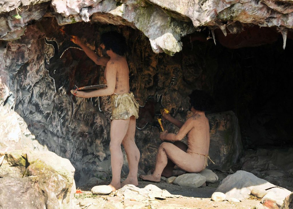 a couple of cave men drawing inside the cave