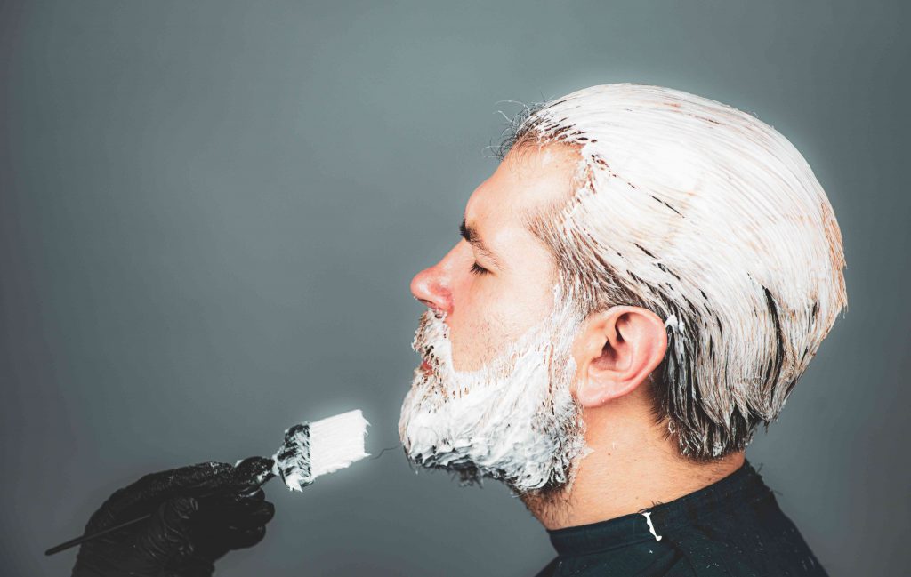 close up of man in saloon, stylist is applying dye on hair and beard of a man 

