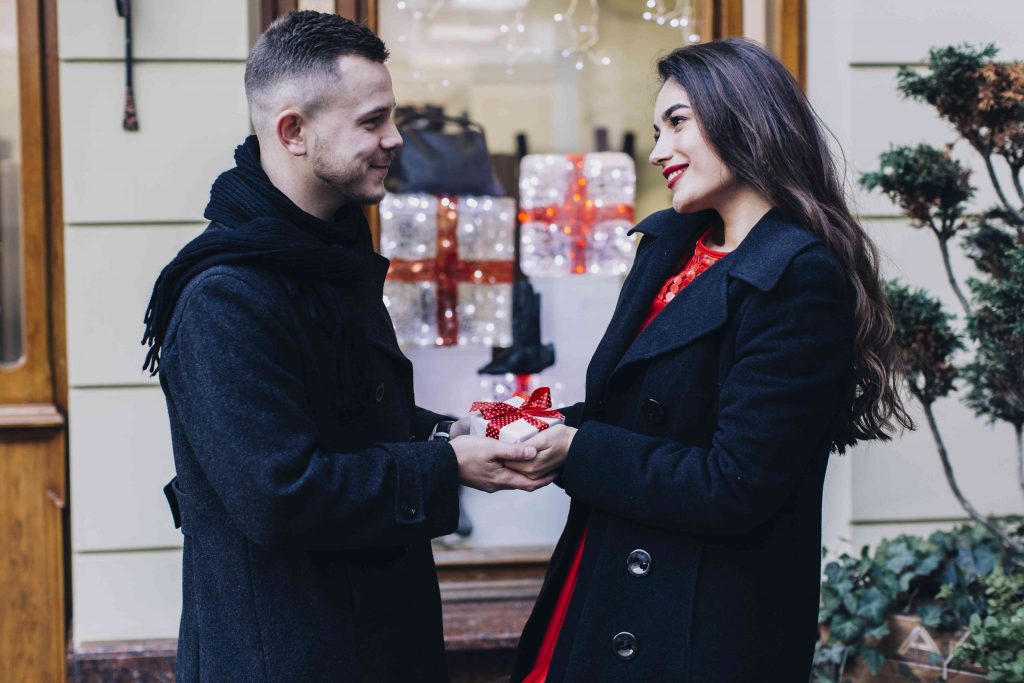 woman gifts man with christmas present and smiles at him 