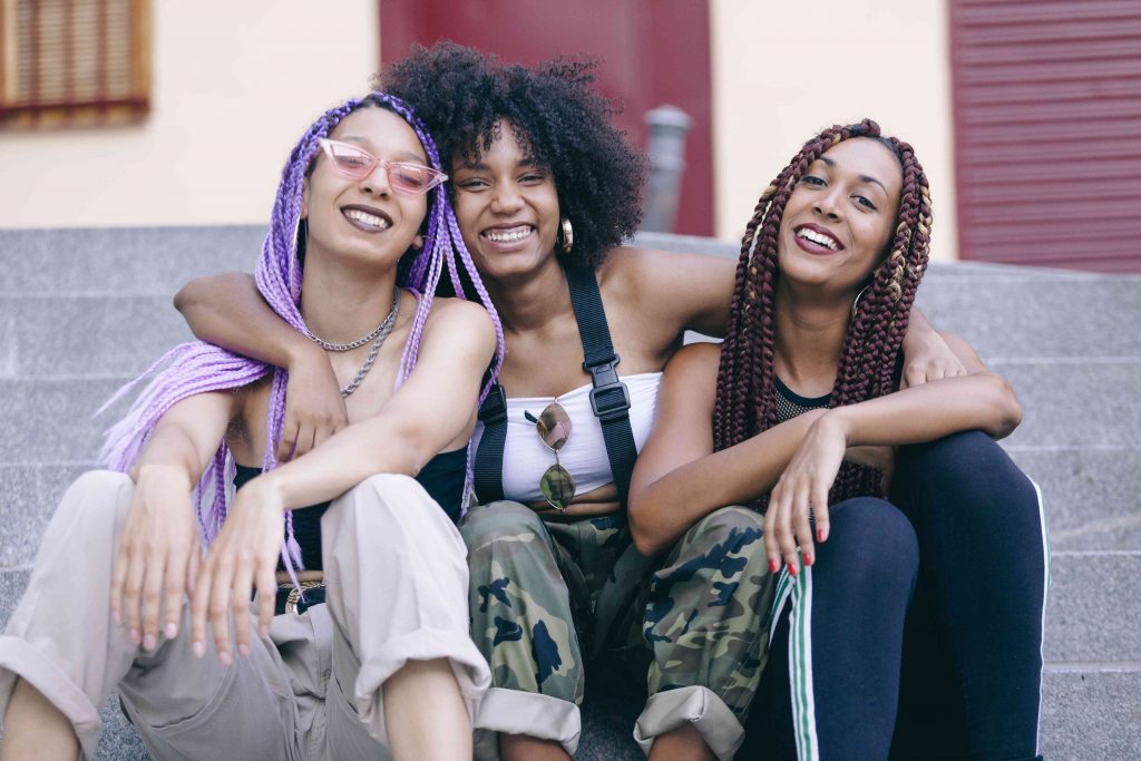 a group of multi-ethnic girls sitting in college campus and smiling with braided hairs in multi colors