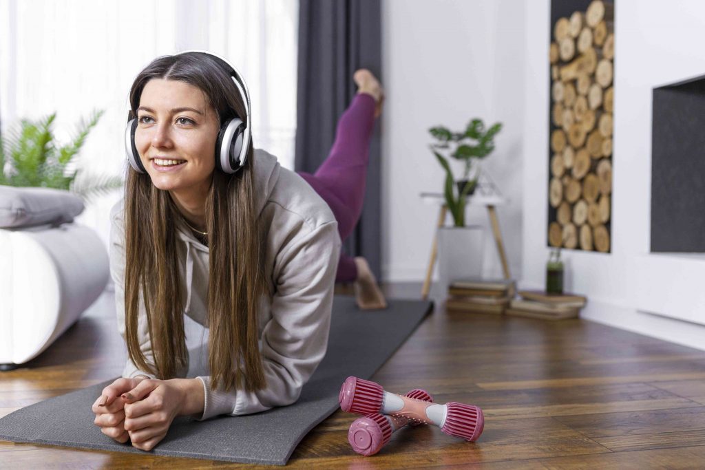 A woman practicing forearm plank while listening to music on head phones in her living room