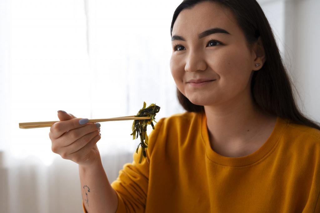 woman having a spoon full of sea weed like wakame and smiling at camera 