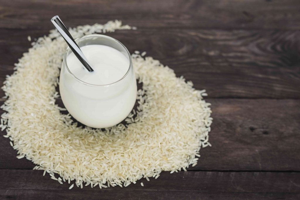 rice scattered on a wooden table and nearby is a glass of white colored rice water