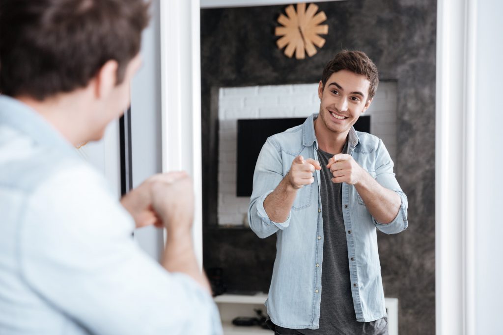 young man stand in front of mirror talks to himself looking at the mirror