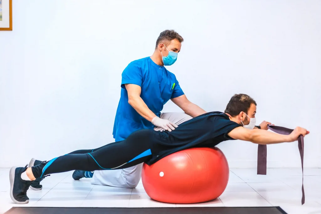 man lying face down on stability ball, while his trainer tests his core muscle endurance