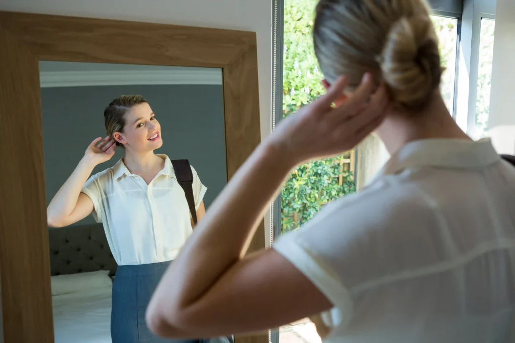 WOMAN STANDS IN FRONT OF MIRROR AND TALKS POSITIVELY TO HERSELF TO IMPROVE HER VIBRATIONAL ENERGY